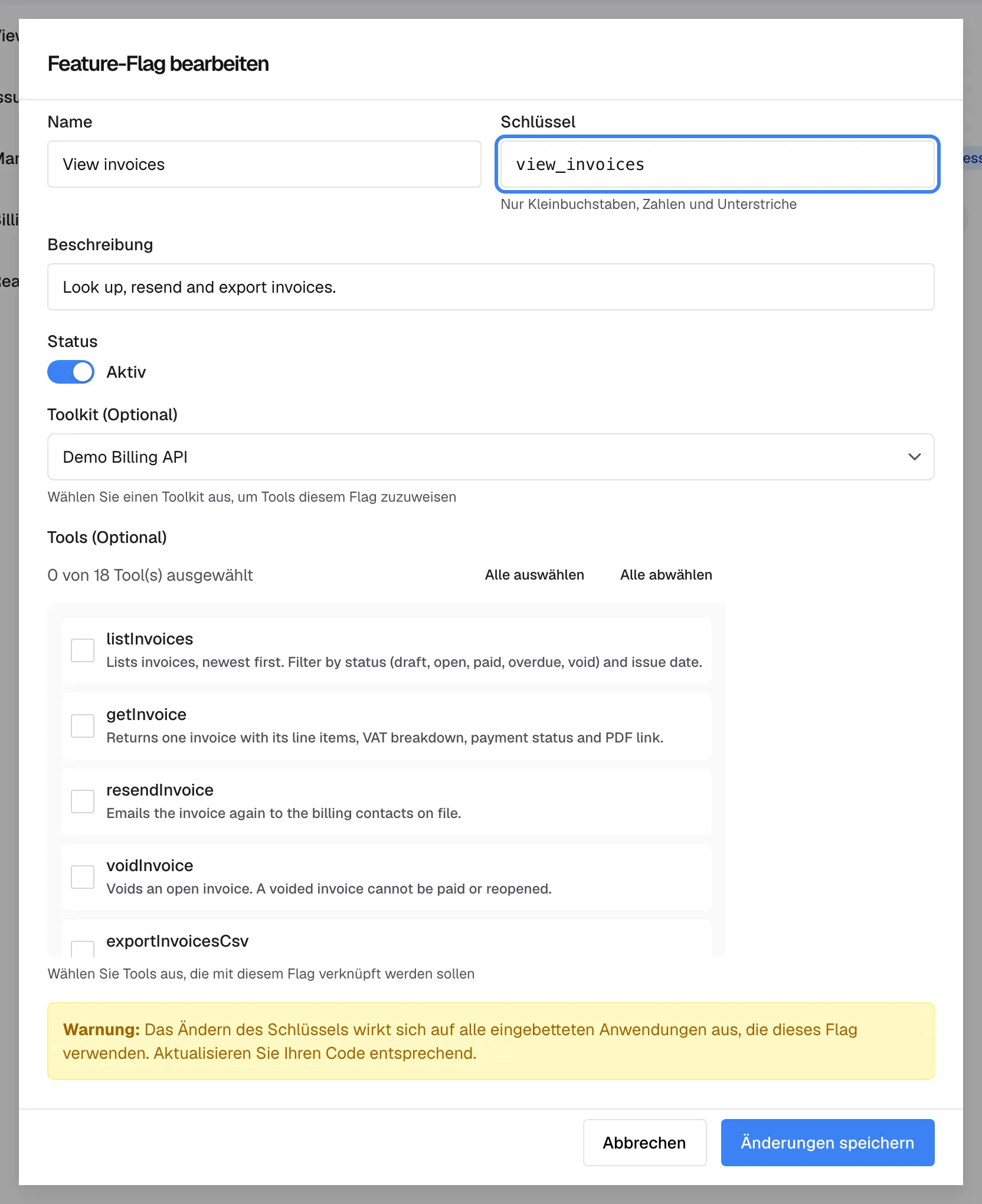 Der Dialog „Feature-Flag bearbeiten“ für die Richtlinie „View invoices“. Das hervorgehobene Feld „Schlüssel“ zeigt view_invoices, den Namen, unter dem die Richtlinie geführt wird. Darunter folgen „Beschreibung“, der Schalter „Status“ auf Aktiv, „Toolkit (Optional)“ mit Demo Billing API und „Tools (Optional)“; der Zähler zeigt „0 von 18 Tool(s) ausgewählt“ und kein Kästchen ist angehakt, obwohl die Liste vier Tools für diese Richtlinie zeigt. Ein Kasten „Warnung:“ weist darauf hin, dass eine Änderung des Schlüssels alle einbettenden Anwendungen betrifft; unten stehen „Abbrechen“ und „Änderungen speichern“.